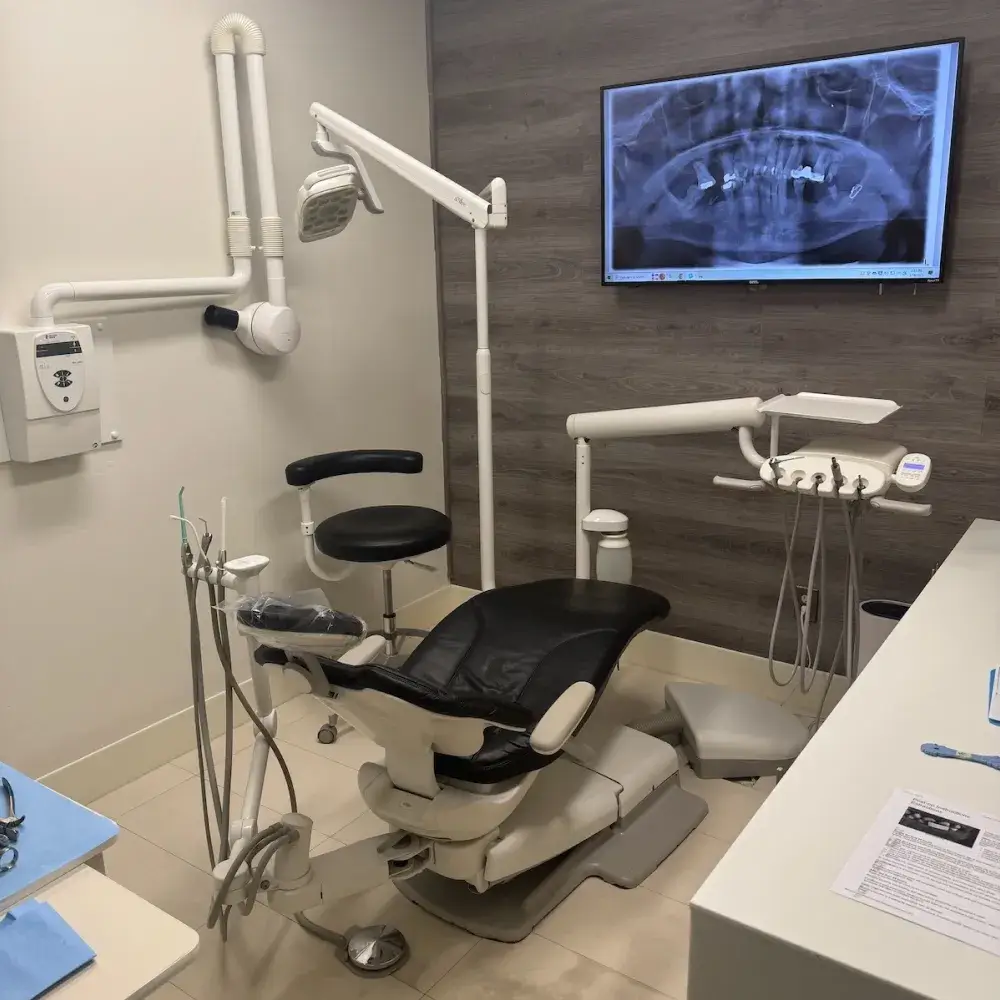 A dental examination room with a chair, dental tools, and an X-ray image on the screen.